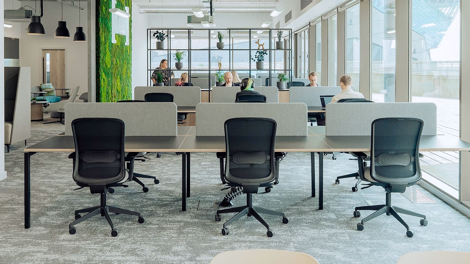 Un plateau de bureaux contemporain : postes alignés, cloisons basses, mur végétal et baies vitrées.